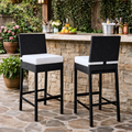 Two black outdoor bar stools with white cushions in front of a stone outdoor bar.