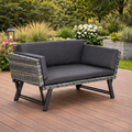 Gray outdoor sofa with dark cushions on a wooden deck surrounded by garden plants.