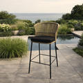 Wicker bar stool with black cushion on a patio with pool and garden view