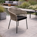 Wicker chair with black cushion on a patio area with plants and furniture in the background