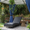Gray lounge chair in a garden setting with blue curtains and plants.