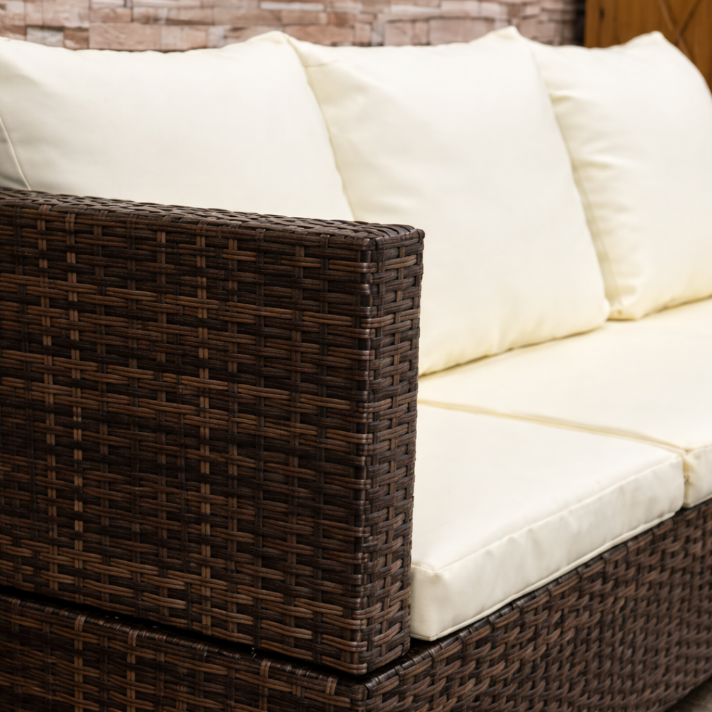 Brown wicker outdoor sofa with white cushions against a wooden wall.
