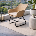 Wicker chair with black legs on a patio with a view of trees and buildings.