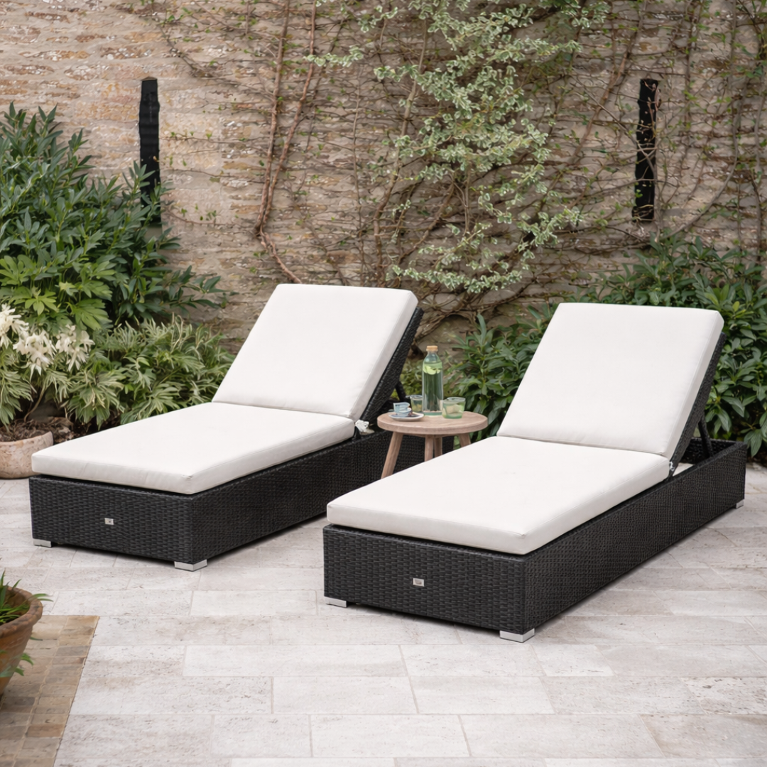 Two black outdoor lounge chairs with white cushions on a patio.